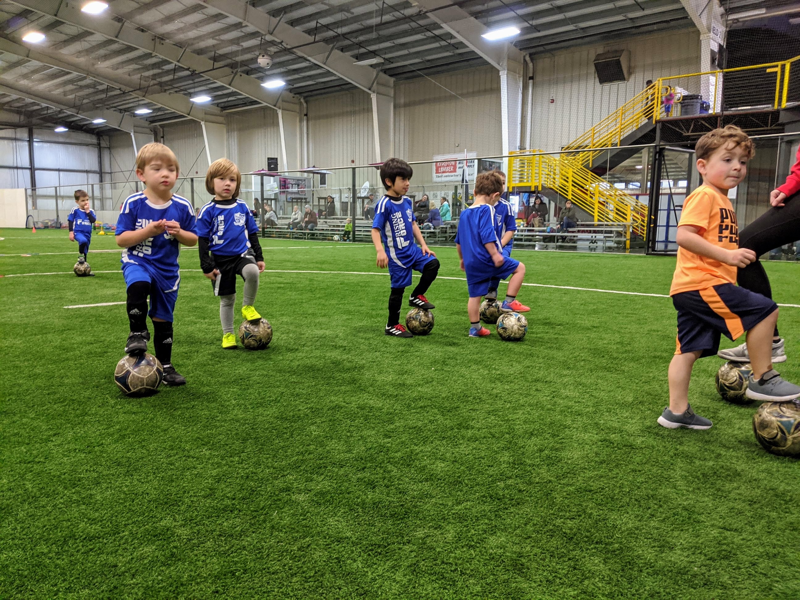 Children, each with one foot on their soccer ball, participating in a Rising Force Academy class at Bremerton Sports Center