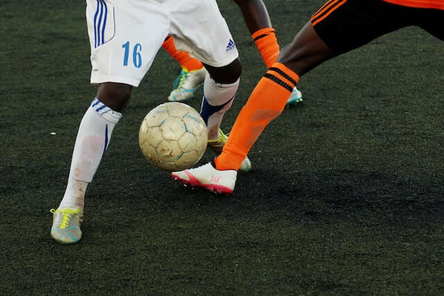 Drop-in soccer match with three sets of players' legs shown going after tattered ball